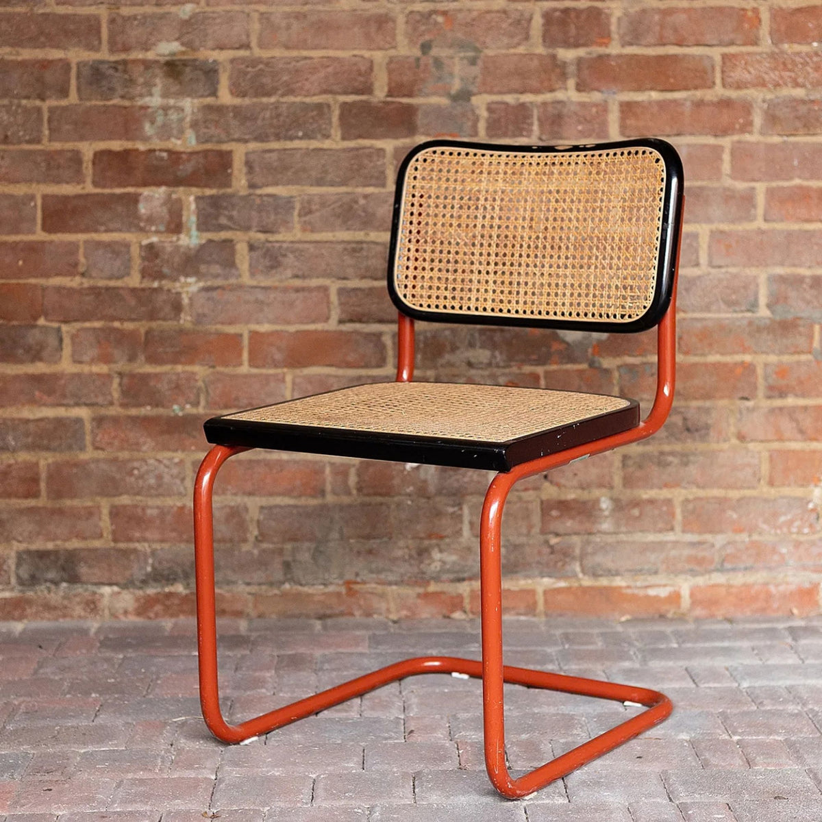 Marcel Breuer style Cesca cantilever dining chair with natural woven cane seat and backrest, black wood frame and red tubular steel cantilever base, ideal for modern dining rooms, cafés, restaurants and contemporary interiors.