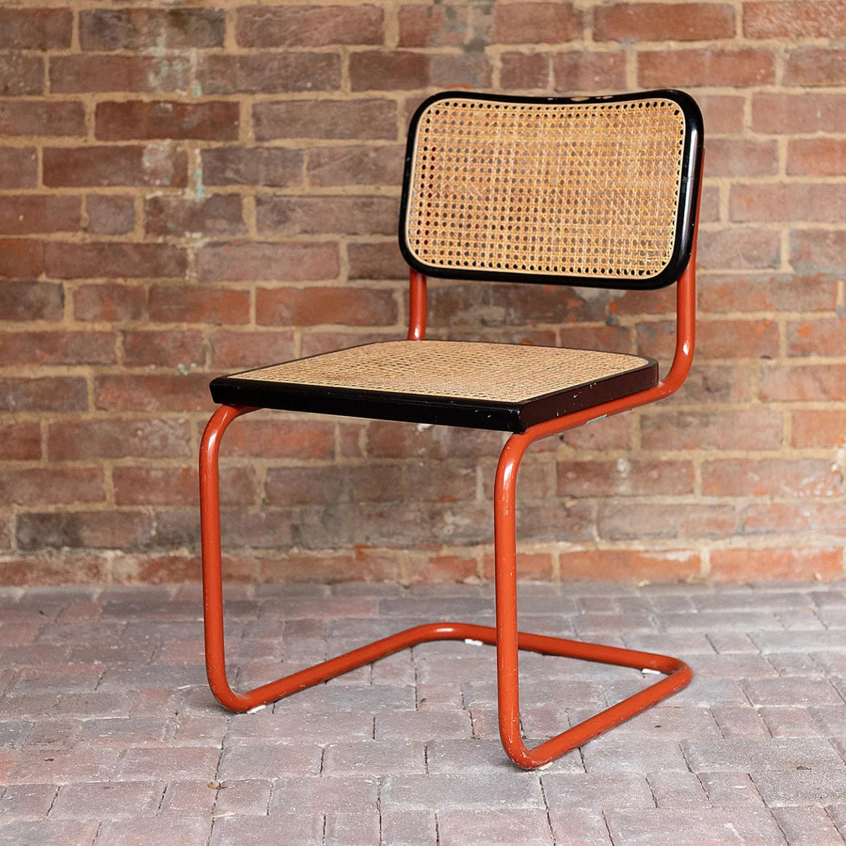 Marcel Breuer style Cesca cantilever chair with natural woven cane seat and backrest, black wood frame and terracotta tubular steel cantilever base, ideal for modern dining rooms, cafés, offices and contemporary interiors.