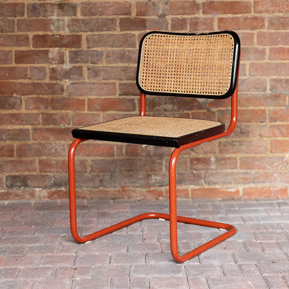 Marcel Breuer style Cesca cantilever chair with natural woven cane seat and backrest, black wood frame and terracotta tubular steel cantilever base, ideal for modern dining rooms, cafés, offices and contemporary interiors.