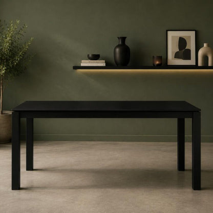 Modern rectangular black dining table with clean-lined legs, styled in a minimalist contemporary dining room with an olive green accent wall, floating shelf, and decorative accessories