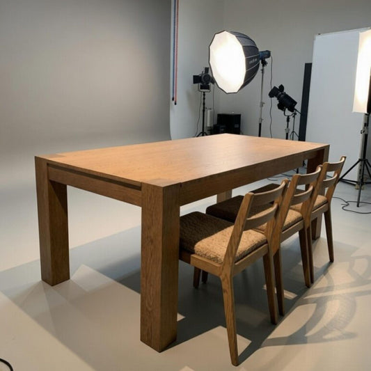 Modern solid oak rectangular dining table with thick square legs, photographed in a professional studio alongside upholstered wooden dining chairs.