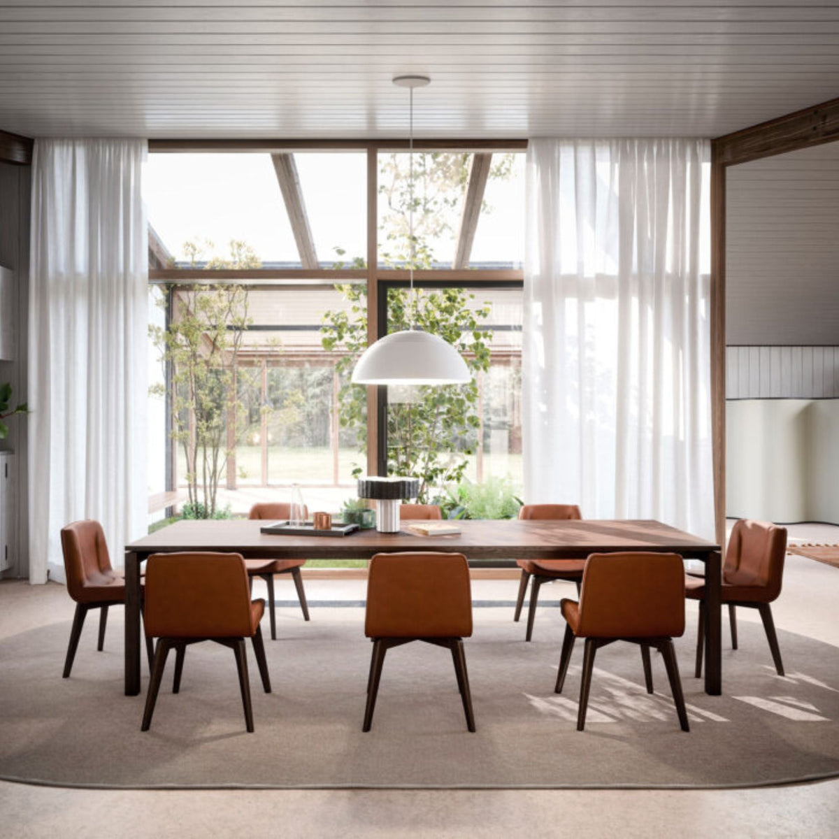 Modern rectangular walnut wood dining table styled with six upholstered dining chairs in a bright contemporary dining room featuring floor-to-ceiling windows and a minimalist pendant light.