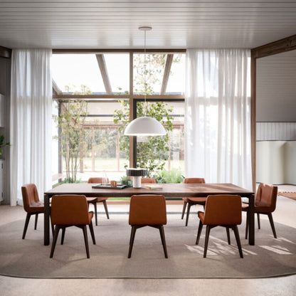 Modern rectangular walnut wood dining table styled with six upholstered dining chairs in a bright contemporary dining room featuring floor-to-ceiling windows and a minimalist pendant light.