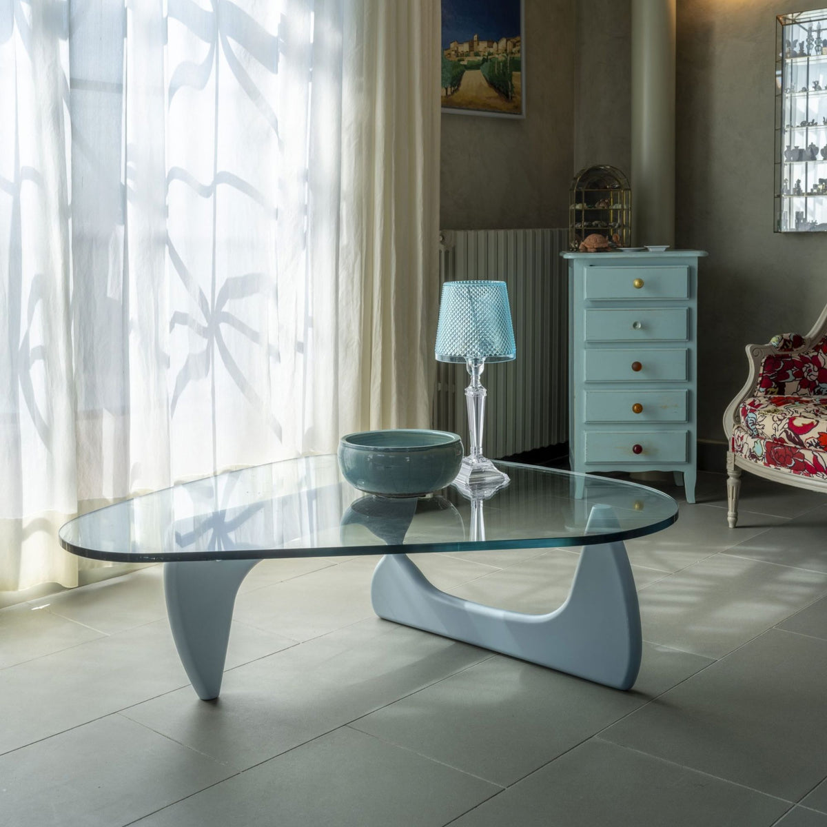 Organic freeform glass coffee table with a sculptural white pedestal base in a contemporary living room, featuring a clear tempered glass top and modern Italian-inspired design.
