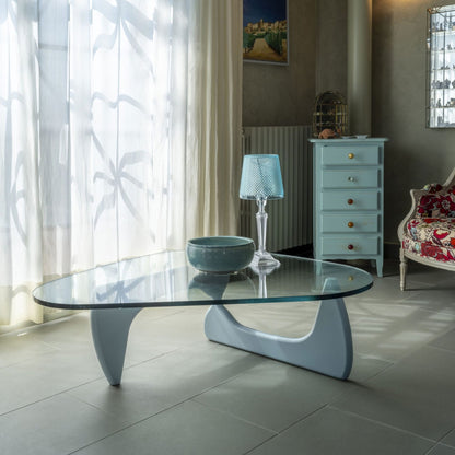 Organic freeform glass coffee table with a sculptural white pedestal base in a contemporary living room, featuring a clear tempered glass top and modern Italian-inspired design.