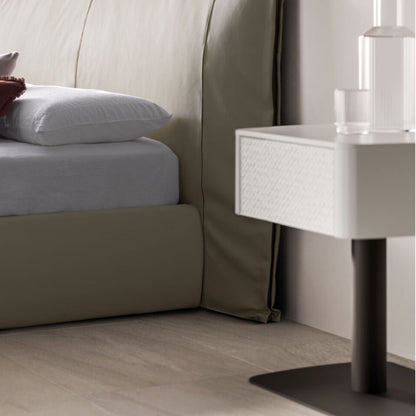 Neatly made bed with white bedding and pillows, next to a modern nightstand.