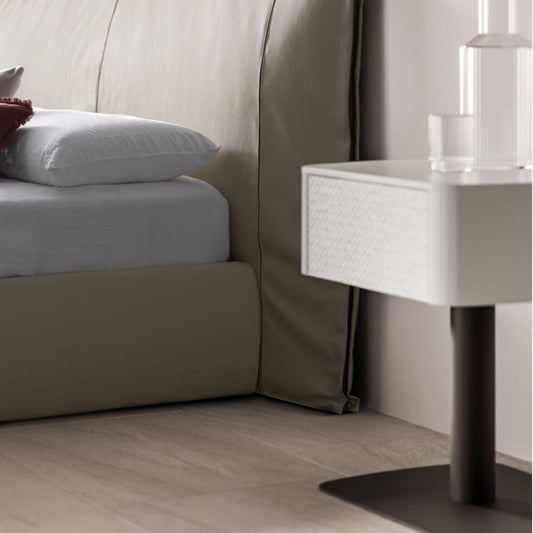 Neatly made bed with white bedding and pillows, next to a modern nightstand.