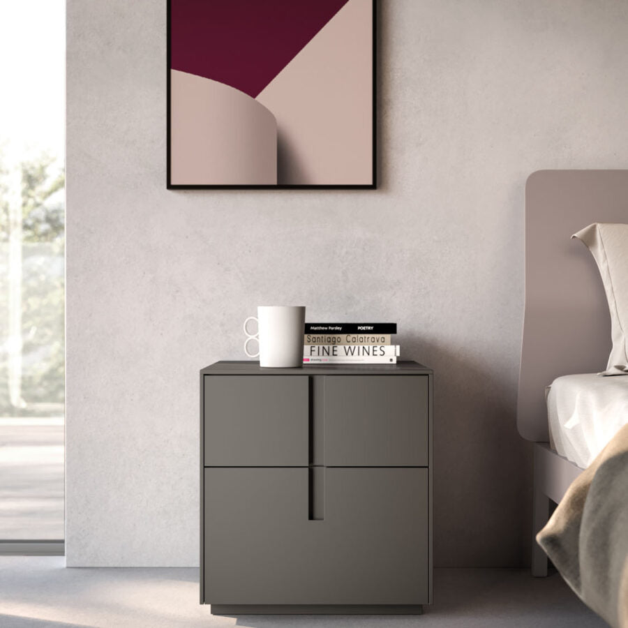 Gray nightstand with a cup and books next to a bed in a bedroom.
