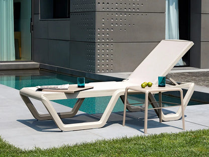 White outdoor sun lounger with an adjustable backrest and matching side table beside a modern swimming pool.
