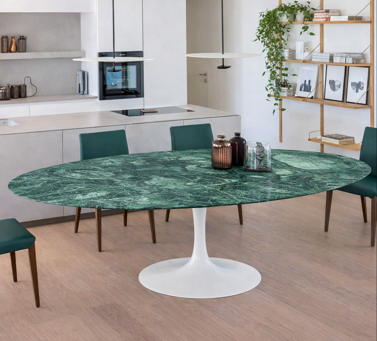 Oval green marble dining table Saarinen style with white pedestal base in a modern kitchen interior, styled with green upholstered chairs, open shelving and minimalist decor