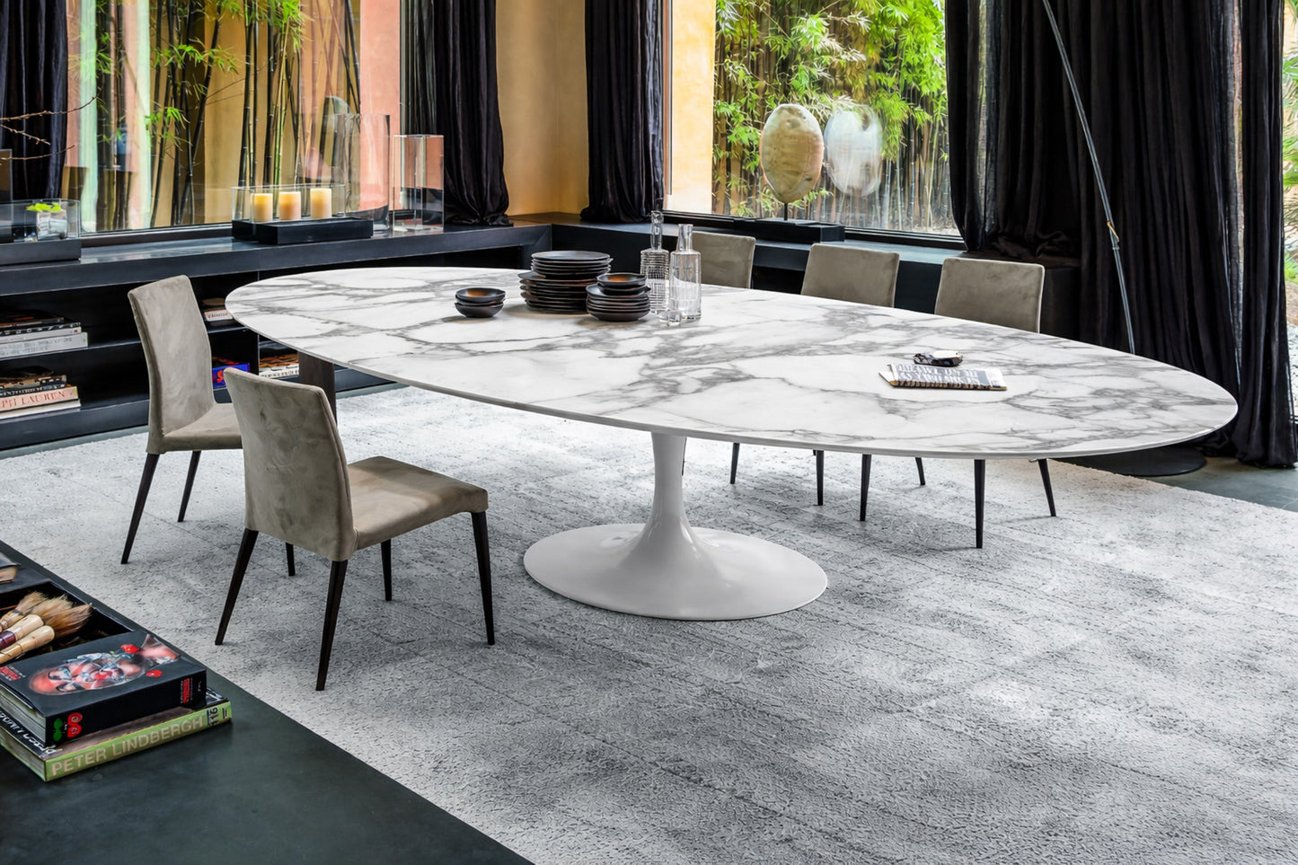 Oval marble dining table with white pedestal base in a modern interior, styled with chairs and tableware, side angle view