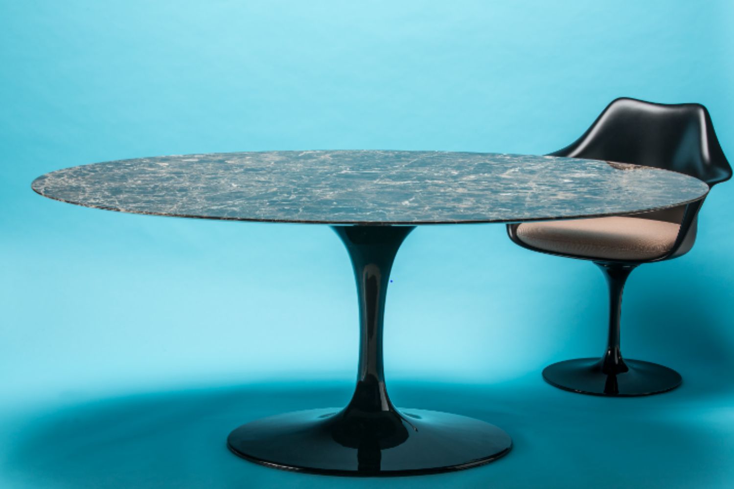 Round dining table with a black pedestal base and a chair on a blue background