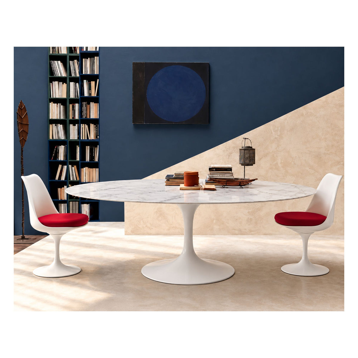 Oval Tulip dining table with a white marble-effect ceramic top and pedestal base, paired with two white chairs with red seat cushions.
