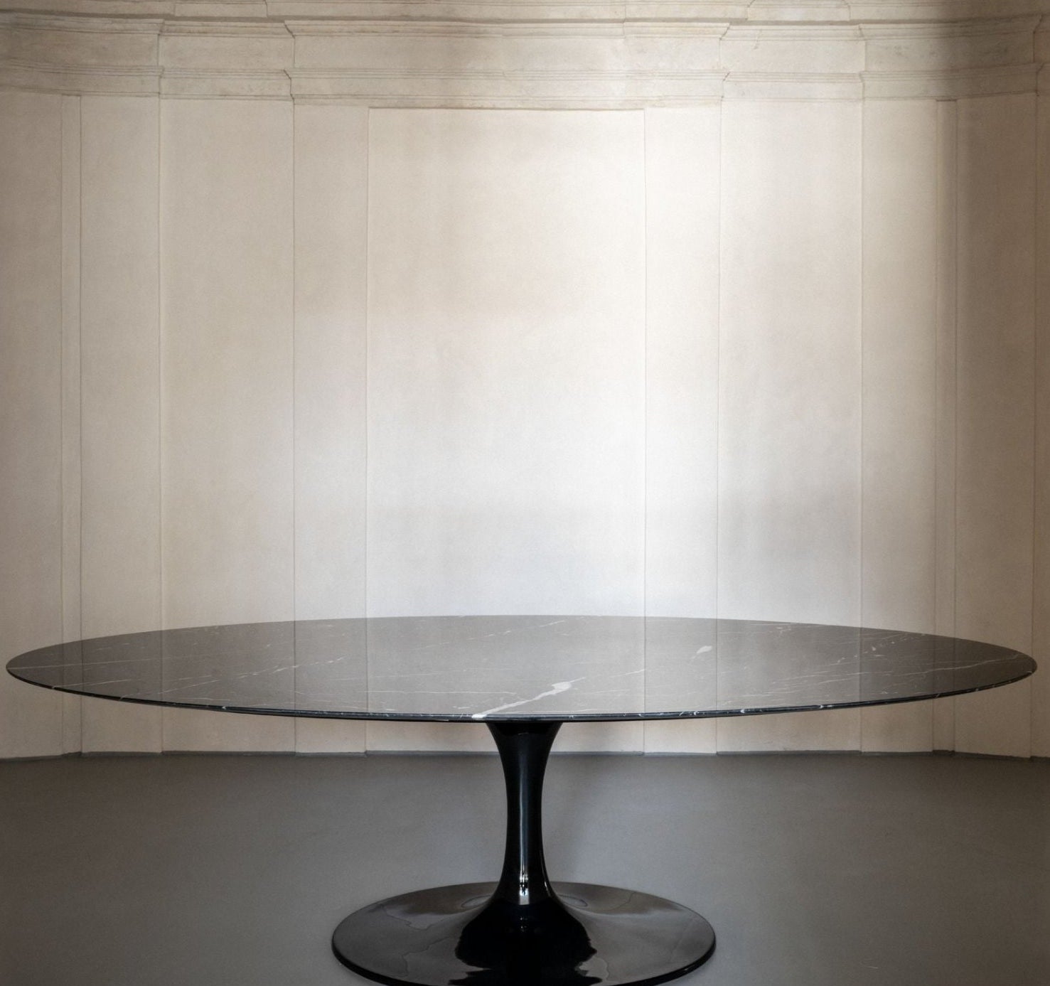 Oval tulip dining table with black marble-effect top and black pedestal base in a minimal interior setting