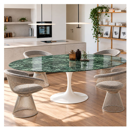 Oval Tulip dining table with a glossy green marble top and white pedestal base, surrounded by woven wire chairs in a modern kitchen.