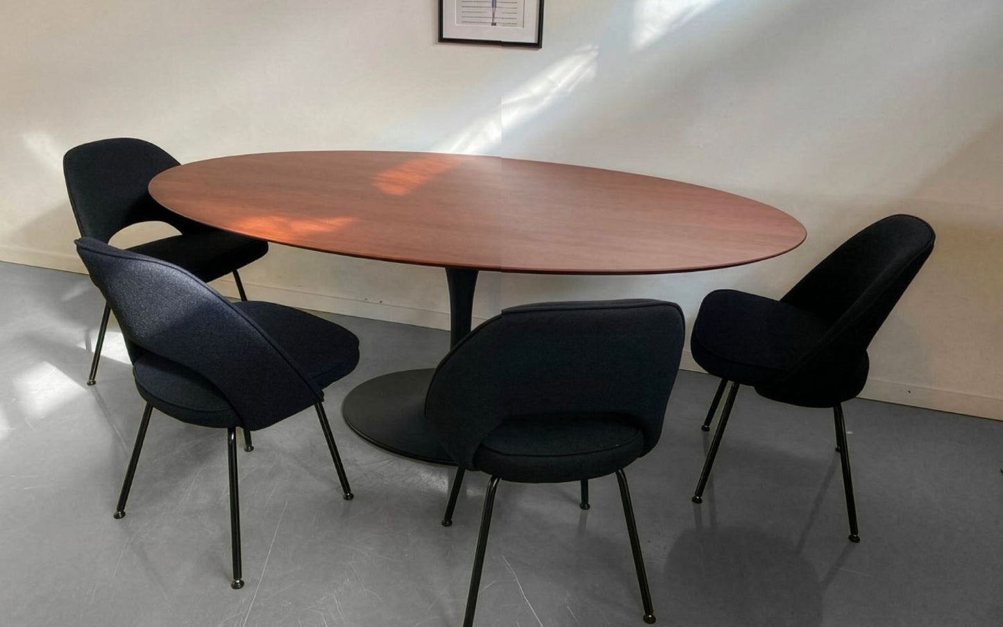 Oval tulip dining table with walnut top and black pedestal base, paired with four upholstered chairs in a minimal interior setting