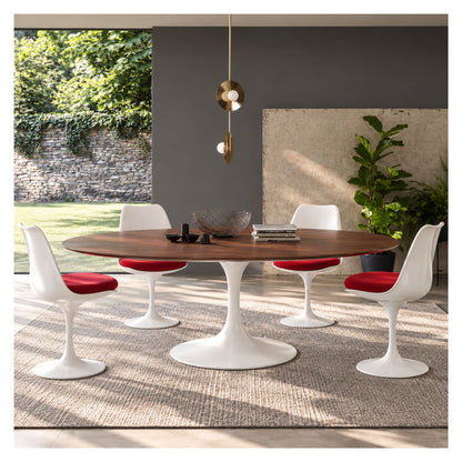 Oval Tulip dining table with a warm wood top and white pedestal base, paired with white chairs and red seat cushions