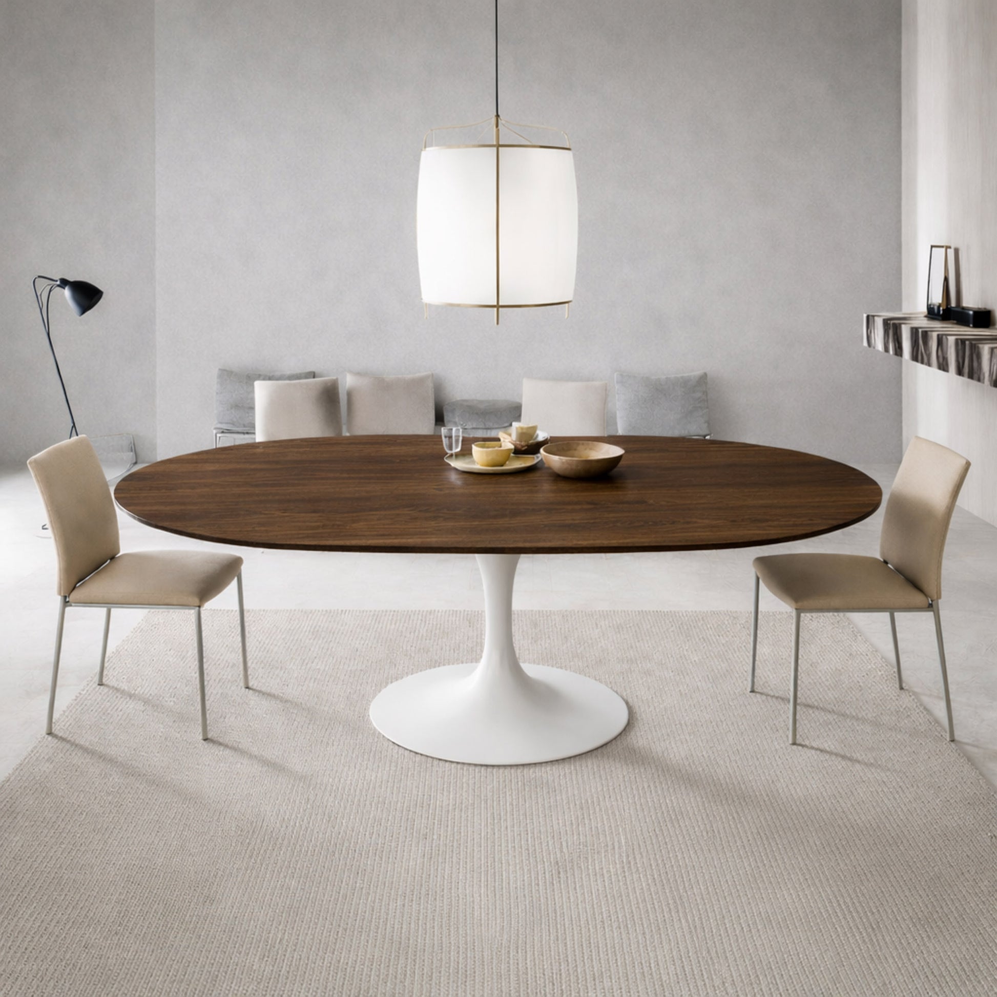 Modern dining room with round walnut tulip dining table and white pedestal base paired with beige upholstered chairs in a minimalist interior