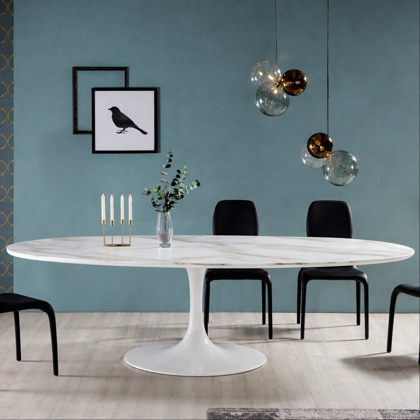 Oval white marble dining table with white pedestal base in a modern dining room Saarinen style, styled with black chairs, blue wall and glass globe pendant lighting