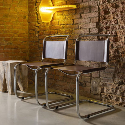 Pair of modern cantilever dining chairs with brown leather seats and backrests on polished chrome tubular frames in a contemporary interior.