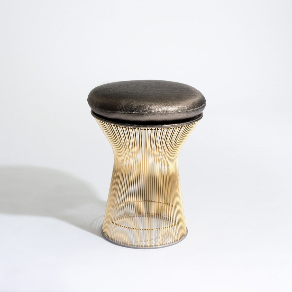 Platner-inspired stool with a gold stainless steel wire frame and round black leather upholstered seat.
