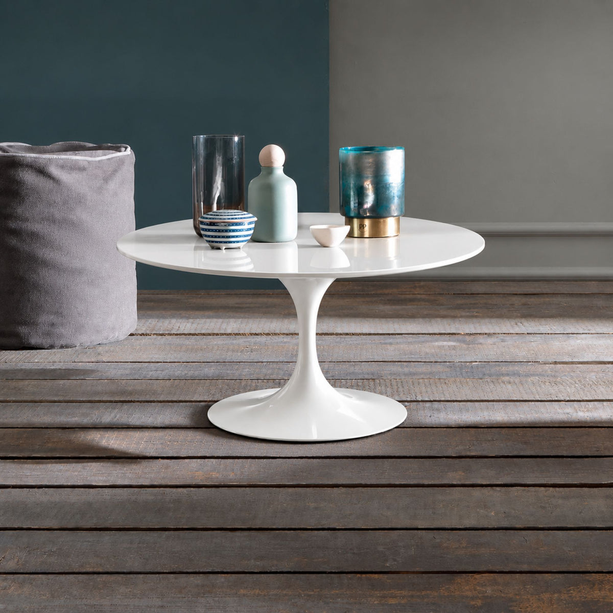 Pure Aura Tulip coffee table featuring a smooth glossy white liquid laminate tabletop paired with a matching glossy white tulip pedestal base. Styled in a modern interior with decorative glass vases, ceramic accessories, and a rustic wooden floor, showcasing timeless Italian-inspired design for contemporary, Scandinavian, and mid-century living spaces.