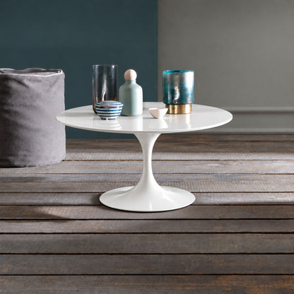 Pure Aura Tulip coffee table featuring a smooth glossy white liquid laminate tabletop paired with a matching glossy white tulip pedestal base. Styled in a modern interior with decorative glass vases, ceramic accessories, and a rustic wooden floor, showcasing timeless Italian-inspired design for contemporary, Scandinavian, and mid-century living spaces.