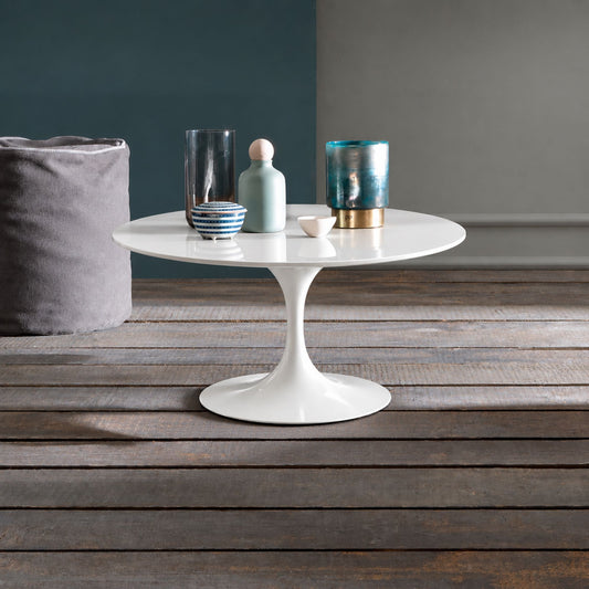 Pure Aura Tulip coffee table featuring a smooth glossy white liquid laminate tabletop paired with a matching glossy white tulip pedestal base. Styled in a modern interior with decorative glass vases, ceramic accessories, and a rustic wooden floor, showcasing timeless Italian-inspired design for contemporary, Scandinavian, and mid-century living spaces.