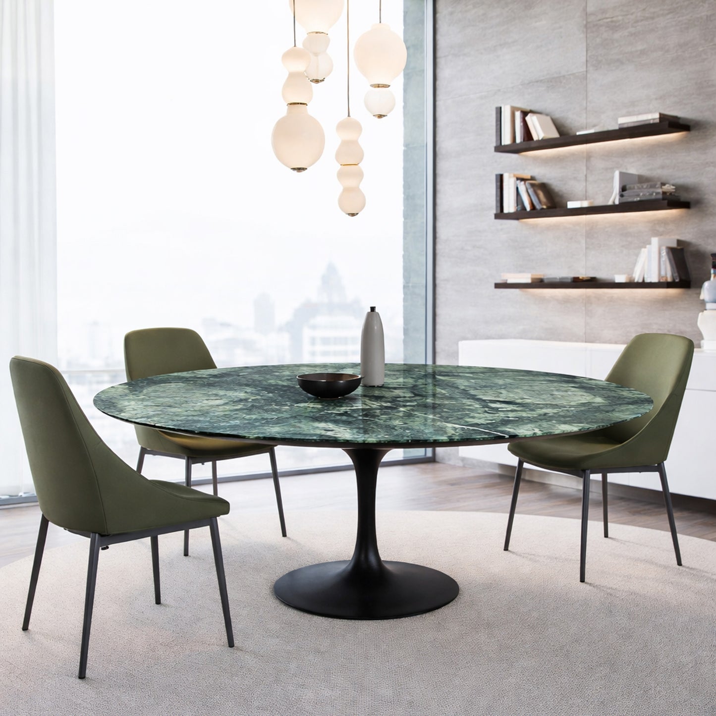 Round green marble dining table with black pedestal base in a modern interior, styled with green upholstered chairs and pendant lighting