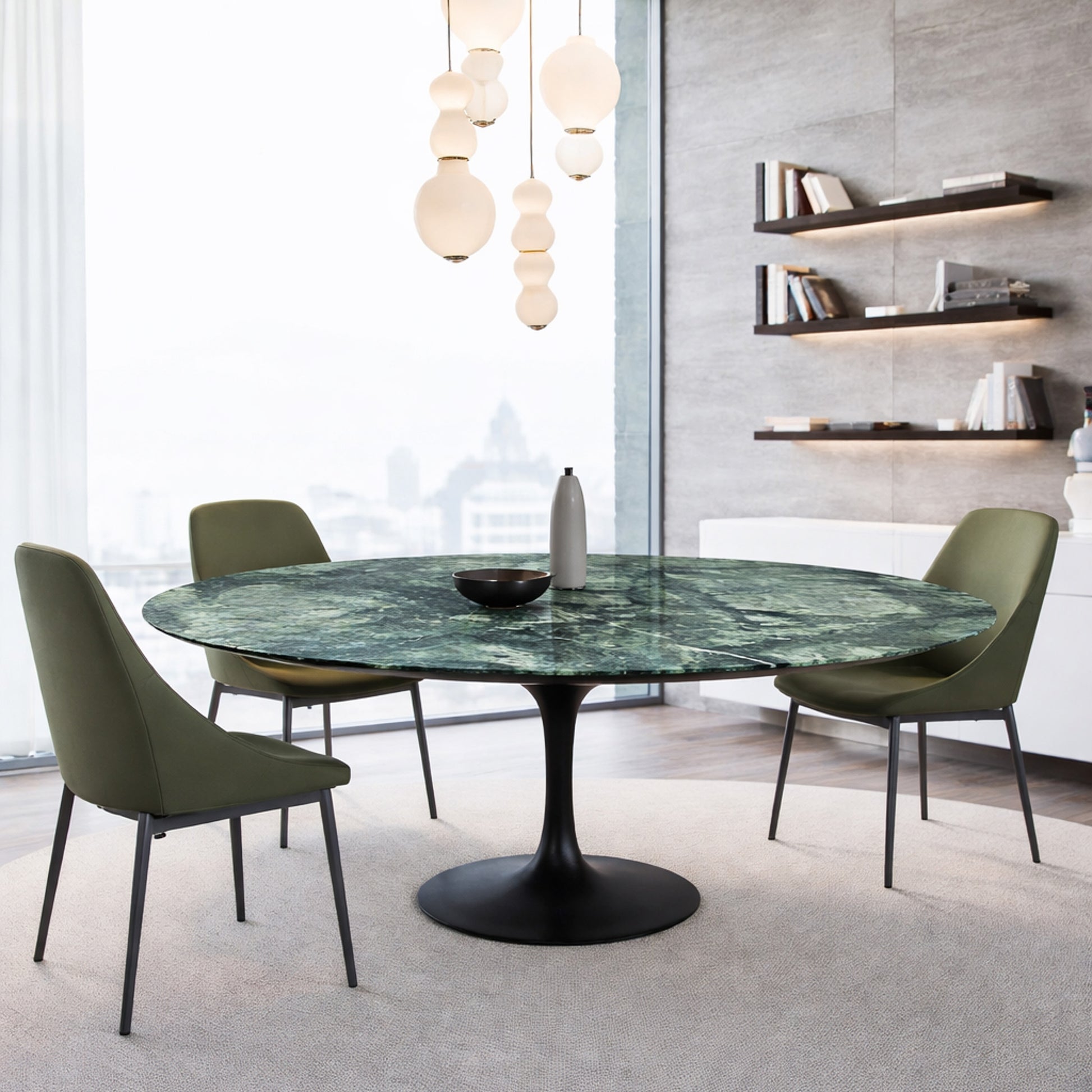 Round green marble dining table with black pedestal base in a modern interior, styled with green upholstered chairs and pendant lighting