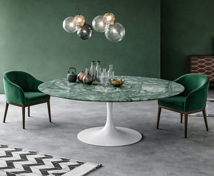 Round green marble dining table with white pedestal base in a modern green interior, styled with green upholstered chairs and glass globe pendant lighting