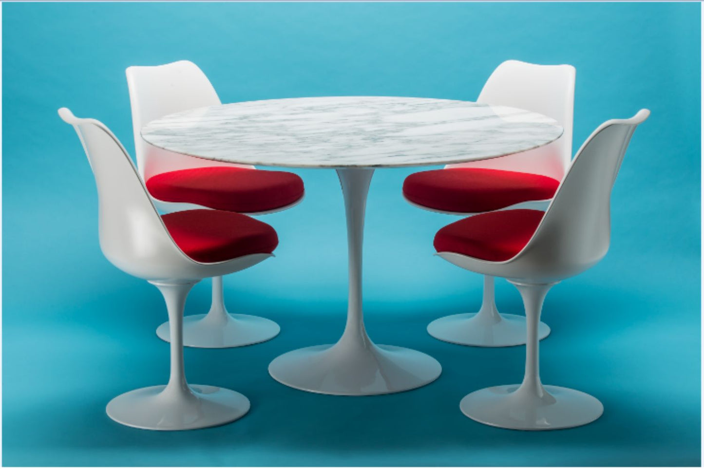 Round marble tulip dining table set with white chairs and red upholstered cushions on blue background