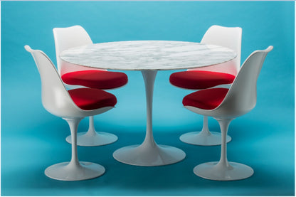 Round marble tulip dining table set with white chairs and red upholstered cushions on blue background