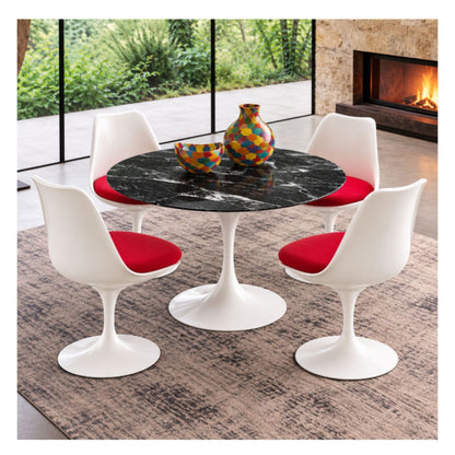 Round Tulip dining table with a black veined marble top and white pedestal base, surrounded by four white chairs with red seat cushions.