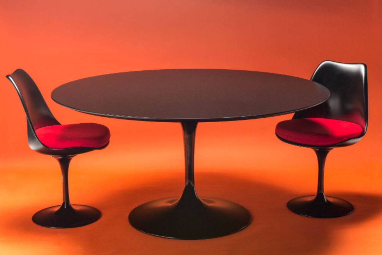 Round tulip dining table set with black laminate top and pedestal base, paired with two upholstered chairs on an orange background
