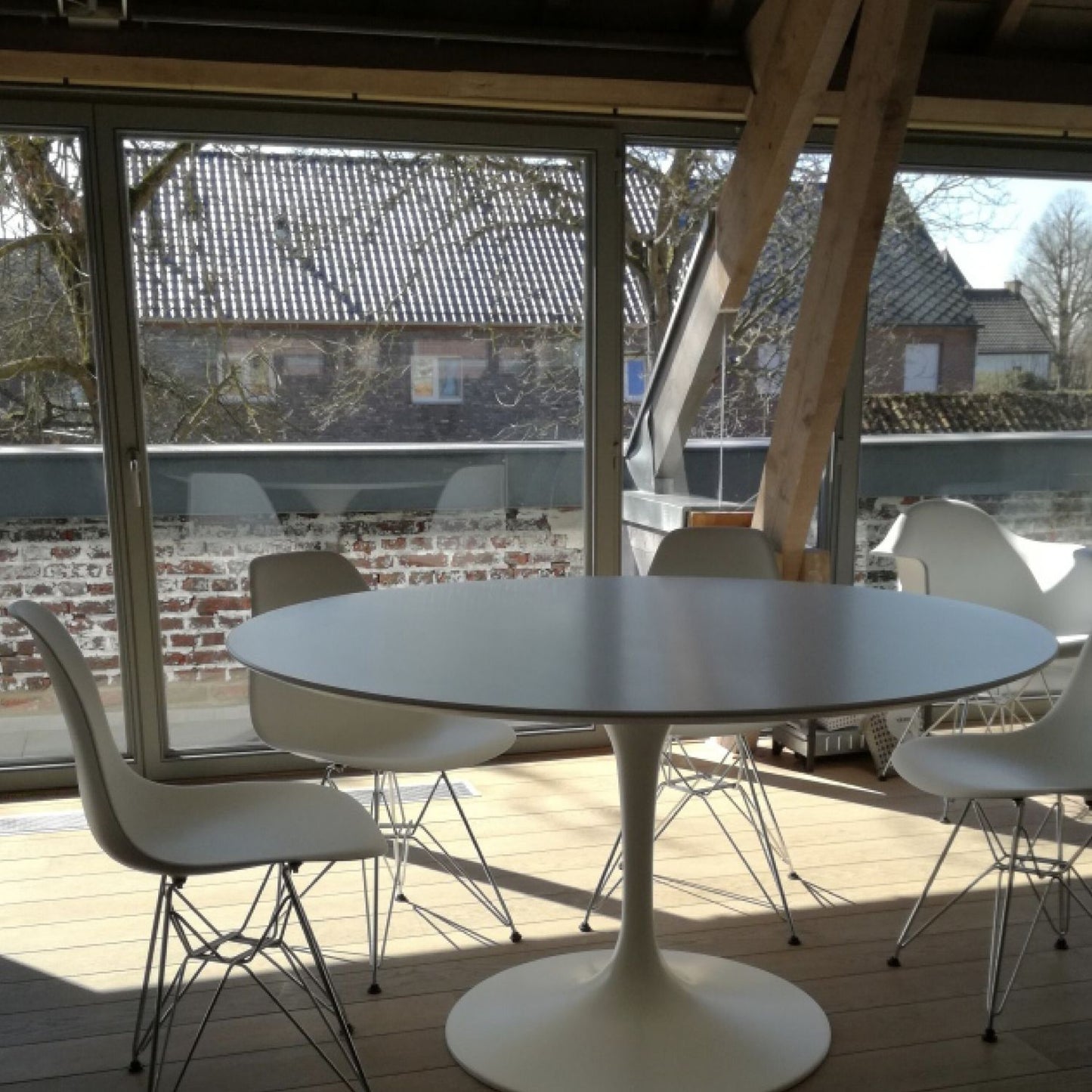 Round tulip dining table with white top and pedestal base, set with four chairs on a wooden deck in an outdoor setting