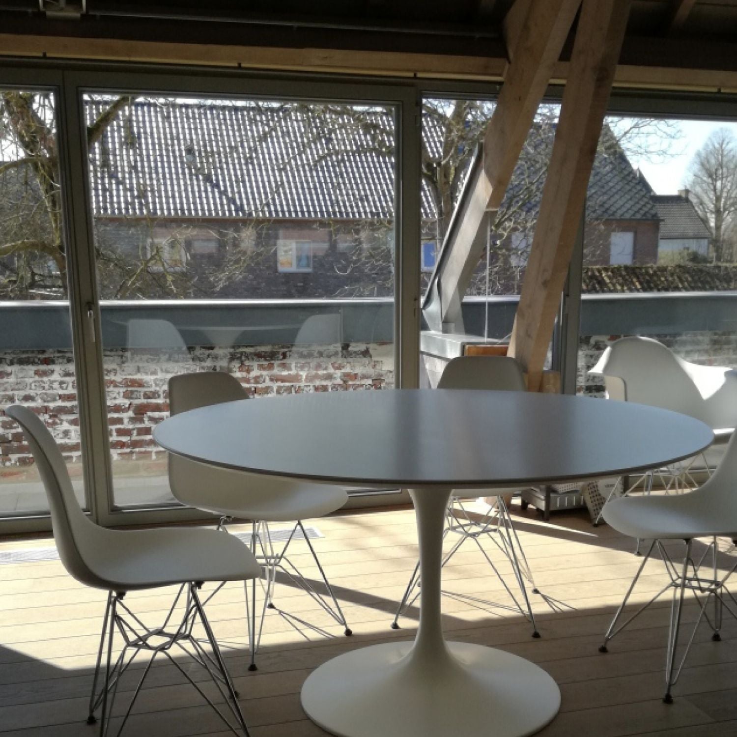 Round tulip dining table with white top and pedestal base, set with four chairs on a wooden deck in an outdoor setting