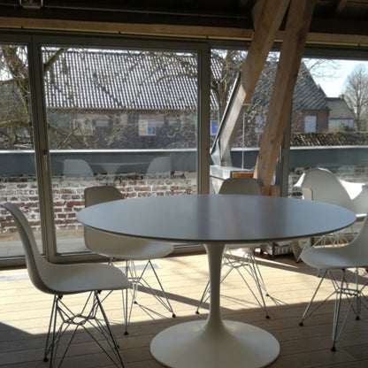 Round tulip dining table with white top and pedestal base, set with four chairs on a wooden deck in an outdoor setting