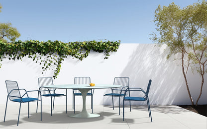 Round tulip outdoor dining table with weather-resistant top and white pedestal base, styled with matching chairs on a modern patio setting