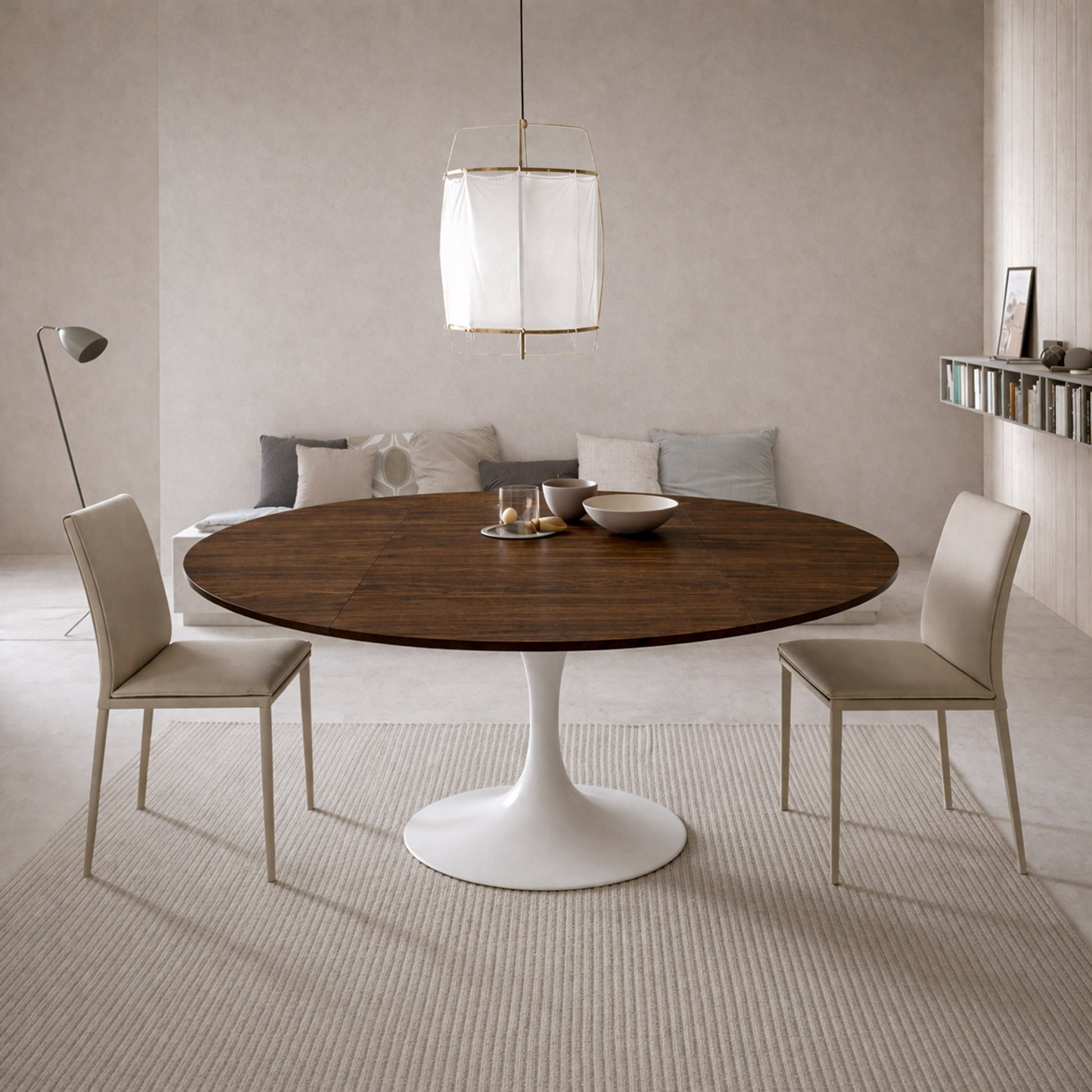 Scandinavian style dining room with round walnut tulip dining table and white pedestal base paired with beige upholstered chairs and neutral minimalist decor