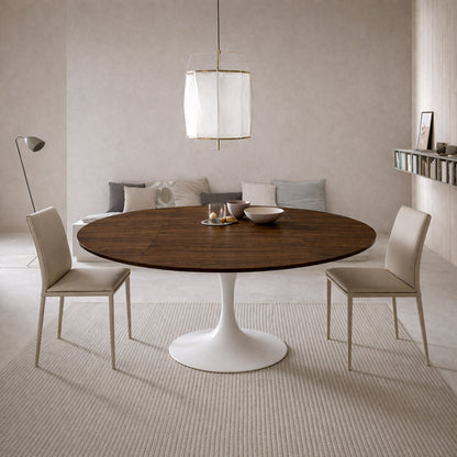 Scandinavian style dining room with round walnut tulip dining table and white pedestal base paired with beige upholstered chairs and neutral minimalist decor