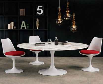 Round white marble dining table with white pedestal base in a dark modern interior, styled with white chairs with red seat cushions, black shelving and glass pendant lighting