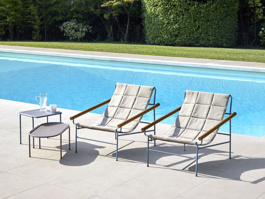 S•CAB Dress Code Glam outdoor armchairs with quilted fabric and iroko wood armrests beside a modern swimming pool, creating a stylish luxury outdoor seating area