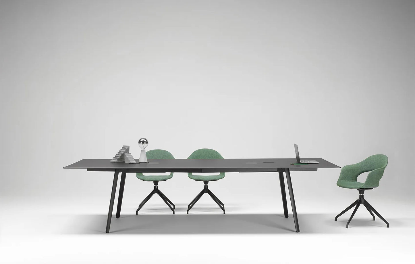 S•CAB Squid OF Office Meeting Table with a black tabletop, integrated cable management, and angled legs in a contemporary conference room with swivel chairs.