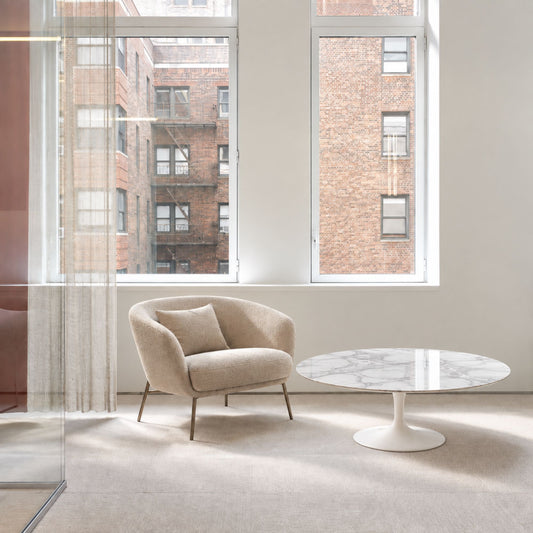 Statuario Loft Tulip coffee table featuring a polished Statuario marble tabletop with elegant grey veining, paired with a glossy white tulip pedestal base. Styled in a bright contemporary living room with a modern lounge chair, floor-to-ceiling windows, and abundant natural daylight. A luxury Italian designer coffee table for modern, Scandinavian, and mid-century interiors.