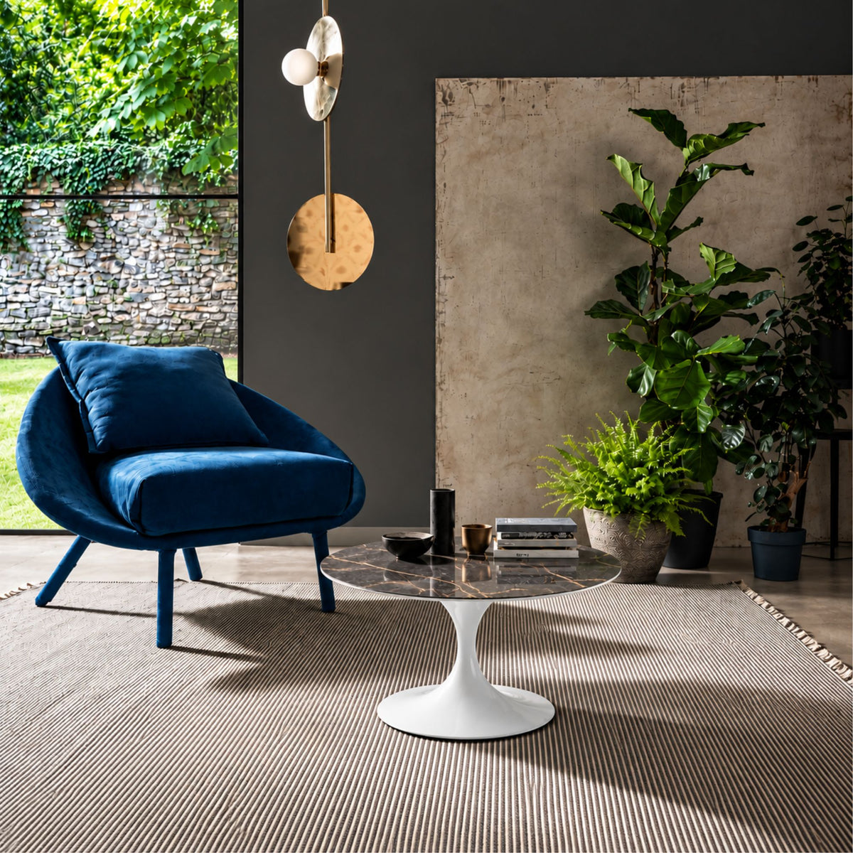 Storm Grey Tulip coffee table featuring a polished grey marble-effect ceramic tabletop with elegant white veining, paired with a glossy white tulip pedestal base. Styled in a contemporary living room with a blue lounge chair, indoor plants, textured rug, and modern wall lighting, showcasing luxury Italian design for modern, Scandinavian, and designer interiors.