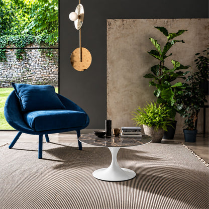Storm Grey Tulip coffee table featuring a polished grey marble-effect ceramic tabletop with elegant white veining, paired with a glossy white tulip pedestal base. Styled in a contemporary living room with a blue lounge chair, indoor plants, textured rug, and modern wall lighting, showcasing luxury Italian design for modern, Scandinavian, and designer interiors.