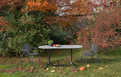 S•CAB Tripé Double Dining Table Base with an oval stone-effect tabletop paired with outdoor chairs in a contemporary garden dining setting.