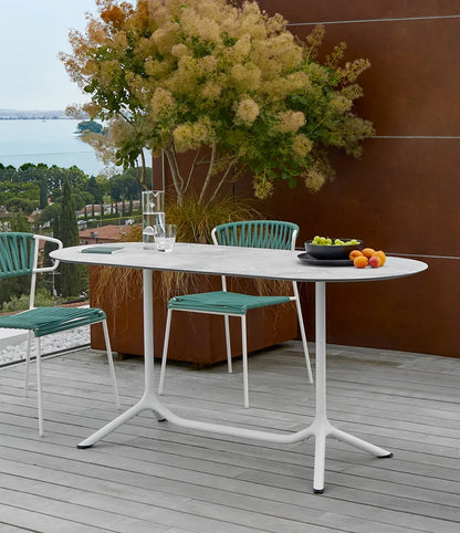 Close-up of the S•CAB Tripé Double Dining Table Base with an oval stone-effect tabletop in a contemporary outdoor dining setting