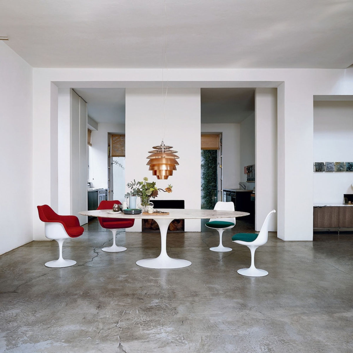 Round Tulip dining table with a white marble top and pedestal base paired with white Tulip dining chairs in red, green and white upholstery in a spacious contemporary dining room, inspired by Eero Saarinen's iconic mid-century modern Pedestal Collection.